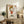 May include: Framed poster featuring a cartoon character with blonde hair wearing a red dress, giving the middle finger with "F*CK U" text above and "YOSHITOMO NARA" below. The artwork is displayed on a rustic wooden sideboard next to a fern plant, pottery vase, and books in a cozy living room setting with neutral tones and natural lighting.