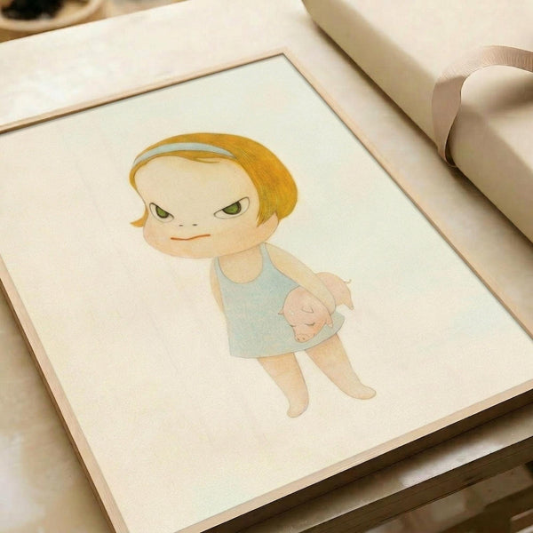May include: A framed art print displaying a cartoon-style illustration of a blonde child with green eyes wearing a light blue sleeveless dress, holding a small pink pig. The artwork has soft pastel colors on cream paper with a light wood frame, shown on a white surface next to cream-colored ribbon.
