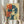 May include: Person in cream ruffled sleeves holding framed vintage-style poster showing woman with dark wavy hair drinking from cup. Artwork features red Japanese characters over blue and cream tones with halftone print effect. Dried pampas grass visible at left, neutral curtain background.