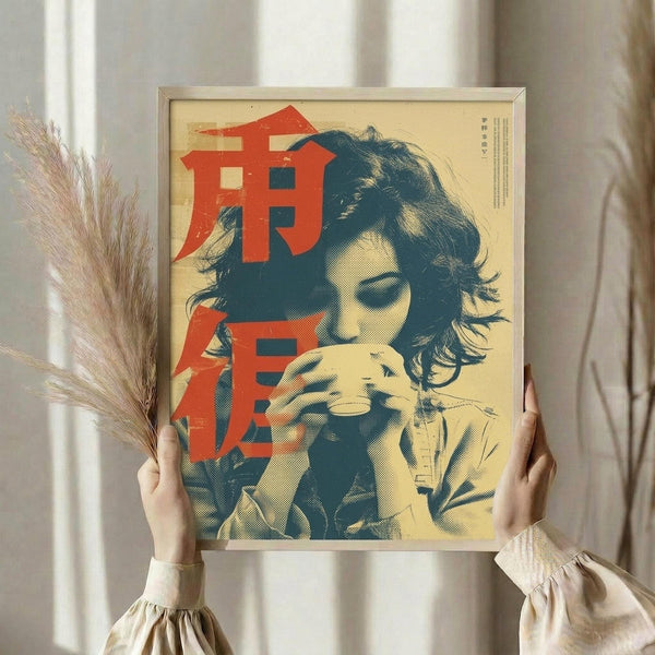 May include: Person in cream ruffled sleeves holding framed vintage-style poster showing woman with dark wavy hair drinking from cup. Artwork features red Japanese characters over blue and cream tones with halftone print effect. Dried pampas grass visible at left, neutral curtain background.