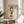 May include: Framed art print displayed on round wooden side table next to beige upholstered chair and potted plant. The poster shows a cartoon-style character with blonde hair wearing red shirt, making an angry expression with raised middle finger. Text reads "FUCK U" at top and "YOSHITOMO NARA" at bottom. Print has thin wooden frame and white matting, positioned in bright room with natural lighting and neutral decor.