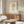 May include: Framed art print displayed on white wall above mid-century walnut credenza in modern living room. Print features cartoon-style character with blonde bob haircut and light blue outfit on cream background. Room has white curved chair, glass coffee table, and minimalist decor with natural lighting.
