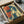 May include: Vintage-style poster print featuring a young woman with curly dark hair drinking from a cup, rendered in retro blue and orange tones on cream background. Framed artwork shown in brown cardboard shipping box with protective tissue paper wrapping and wooden corner guards for safe packaging.