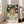 May include: Art nouveau style poster in light wood frame leaning against white wall next to beige sofa. Features woman with flowing auburn hair surrounded by white daisies against dark teal starry background. She wears flowing white dress and gazes upward. Text reads "MARGUARITE" with Japanese characters and museum exhibition details from 1972 Tokyo. Natural lighting streams through windows in minimalist living room setting.