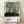 May include: Framed art print featuring abstract forest scene with tall black tree trunks, dotted green circles, and speckled ground in muted green, cream and black tones. Japanese text below reads "YAYOI KUSAMA" with Tokyo, Japan 1984 and color palette swatches. Light wood frame leaning against white wall on natural wood flooring with soft shadows.