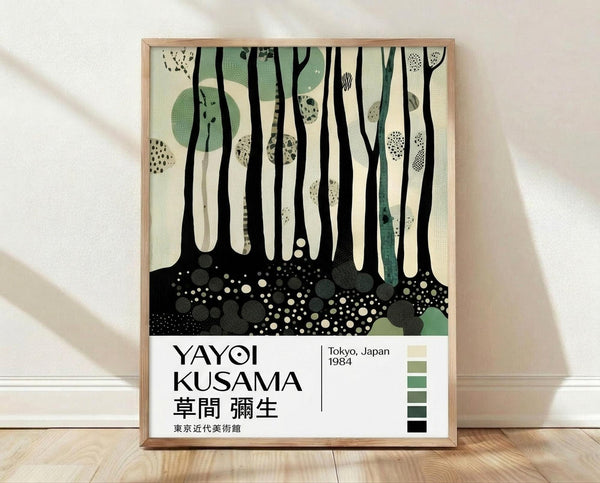 May include: Framed art print featuring abstract forest scene with tall black tree trunks, dotted green circles, and speckled ground in muted green, cream and black tones. Japanese text below reads "YAYOI KUSAMA" with Tokyo, Japan 1984 and color palette swatches. Light wood frame leaning against white wall on natural wood flooring with soft shadows.