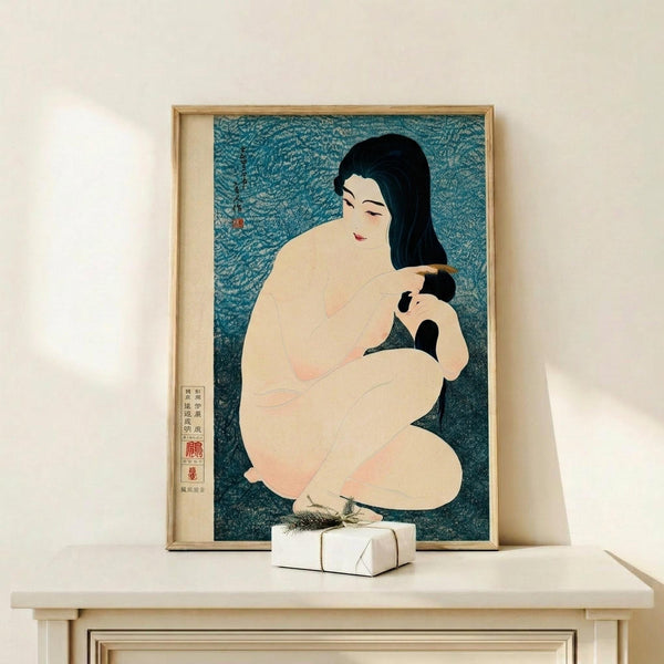 May include: Framed Japanese woodblock print featuring a nude woman with black hair combing her dark hair against a textured blue-green background, displayed on a light wood shelf beside a small wrapped gift with natural twine and dried grass accent, set against a cream colored wall.