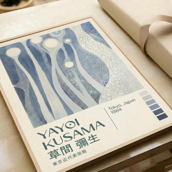 May include: Framed art print featuring abstract blue and white organic flowing patterns with dotted textures, displayed on white bedding next to a beige pillow. The poster shows Japanese text at bottom with "Tokyo, Japan 1984" and color swatches. The artwork has fluid, wave-like forms in various shades of blue against cream background, presented in a thin light wood frame.