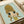 May include: Framed art print featuring anime-style illustration of young girl with long wavy blonde hair and large dark eyes, wearing yellow top against soft mint green background. Print sits on white bedding next to cream ribbon, showing warm natural lighting and delicate artistic style with soft color palette.