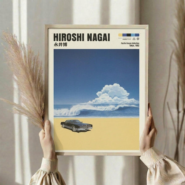 May include: Person in cream sweater holding framed poster print against white curtained window. Artwork shows vintage dark car on golden beach with blue ocean waves and puffy white clouds against deep blue sky. Natural wood frame, held alongside dried pampas grass stems. Clean, minimalist styling with soft natural lighting.