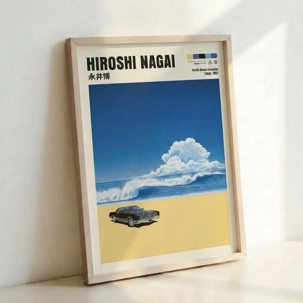 May include: Framed poster print leaning against white wall showing retro-style artwork with blue ocean waves, fluffy white clouds, yellow sandy beach, and dark vintage car. Features "HIROSHI NAGAI" text at top with Japanese characters below. Light wood frame surrounds the vibrant coastal scene with clear blue sky gradient.