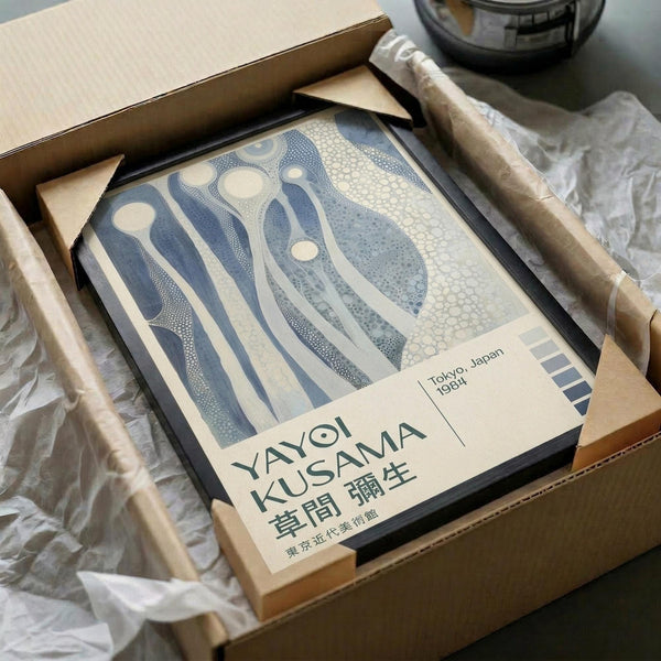 May include: Framed poster with abstract blue and cream flowing organic shapes in dotted pattern style, packed in cardboard shipping box with protective wrapping paper and wooden frame corners visible, sitting on white fabric surface next to dark glass vessel