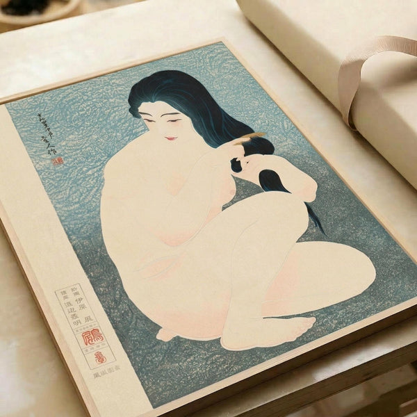 A Japanese woodblock print showing a nude woman with long black hair combing or styling her hair against a textured blue-green background. The artwork features soft, muted colors in traditional ukiyo-e style with Japanese text and red seal stamps. The print is displayed in an open book or portfolio with cream-colored pages on a light surface.