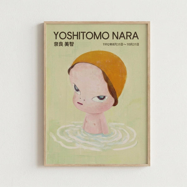 Framed poster featuring a stylized illustration of a child-like figure with an oversized head, orange bowl-cut hair, and large eyes, emerging from concentric ripples in pale green water. The artwork has a soft, dreamy quality with muted colors on a light green background. Text at the top reads "YOSHITOMO NARA" with Japanese characters and exhibition dates from 1992. The poster is displayed in a natural wood frame against a white wall.