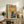 May include: Framed vintage-style poster featuring a woman in yellow shirt and blue skirt holding a katana sword, with red Japanese text on cream background. Displayed on rustic wooden sideboard alongside books, ceramic vase, and fern plant in neutral-toned living room setting.