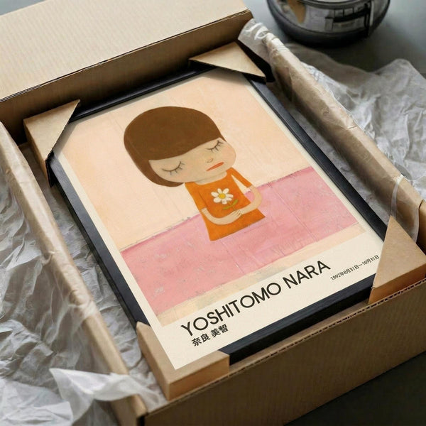 May include: Framed art print featuring a minimalist illustration of a young girl with brown bob haircut and closed eyes, wearing an orange top with white flower design, sitting on pink checkered surface against cream background. Black frame sits in opened cardboard shipping box with white tissue paper padding.