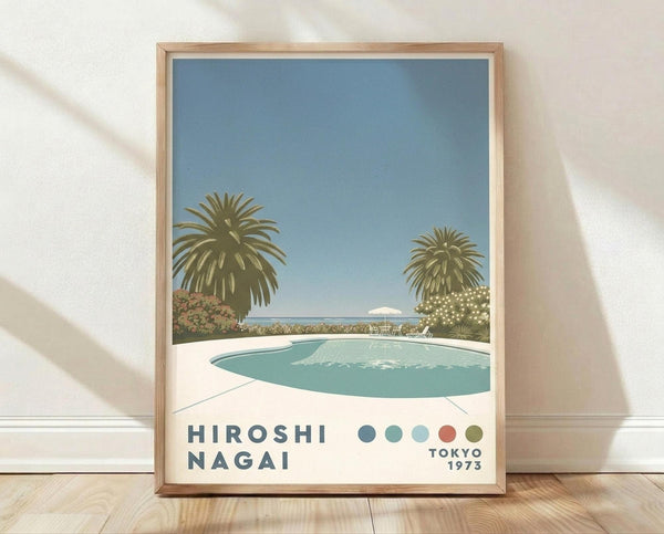 May include: Framed poster print leaning against white textured wall on light wood floor. Artwork shows retro-style illustration of turquoise swimming pool surrounded by white concrete, two large palm trees, and flowering bushes under blue sky. Text reads "HIROSHI NAGAI" and "TOKYO 1973" with colored dots in blue, coral, and olive green. Natural wood frame, soft shadows from window light.