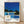 May include: Framed poster print leaning against white wall on wooden floor. Artwork shows modernist poolside scene with glass house, blue swimming pool, yellow lounge chairs, palm trees against deep blue sky. White frame with natural wood border. Features "HIROSHI NAGAI" text and "TOKYO 1973" with colorful dots below illustration.