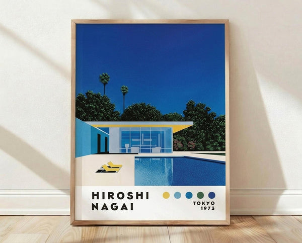 May include: Framed poster print leaning against white wall on wooden floor. Artwork shows modernist poolside scene with glass house, blue swimming pool, yellow lounge chairs, palm trees against deep blue sky. White frame with natural wood border. Features "HIROSHI NAGAI" text and "TOKYO 1973" with colorful dots below illustration.