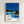May include: Framed poster print hanging on white textured wall showing mid-century modern poolside scene with glass house, swimming pool, yellow lounge chair, palm trees against bright blue sky. Wood frame surrounds artwork featuring clean geometric architecture, lush green landscaping, and color palette dots below black text reading "HIROSHI NAGAI" and "TOKYO 1973" in minimalist design style.
