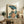 May include: Framed Japanese woodblock print artwork featuring a woman in colorful kimono holding a blue parasol, surrounded by large teal lotus leaves. The vintage-style print is displayed on a rustic wooden sideboard next to a fern plant, ceramic vase, and books in a neutral-toned living room setting with beige chair visible.