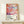May include: Framed art poster featuring abstract colorful fish swimming in coral and pink tones with dotted patterns, displayed on light wood shelf next to small wrapped gift box with evergreen sprig. Poster shows Japanese text and Tokyo 1984 with color palette squares. Warm neutral wall background.