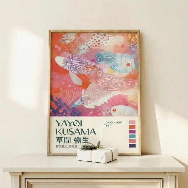 May include: Framed art poster featuring abstract colorful fish swimming in coral and pink tones with dotted patterns, displayed on light wood shelf next to small wrapped gift box with evergreen sprig. Poster shows Japanese text and Tokyo 1984 with color palette squares. Warm neutral wall background.
