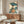 May include: Japanese woodblock print artwork displayed in modern living room setting, featuring woman in colorful kimono holding blue parasol surrounded by large leaves. Print shown in thin frame above wooden sideboard with white table lamp and brass floor mirror. White curved chair and glass coffee table visible in foreground on light wooden floors.