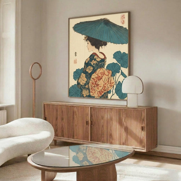 May include: Japanese woodblock print artwork displayed in modern living room setting, featuring woman in colorful kimono holding blue parasol surrounded by large leaves. Print shown in thin frame above wooden sideboard with white table lamp and brass floor mirror. White curved chair and glass coffee table visible in foreground on light wooden floors.