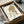 May include: Framed art print of a cartoon-style girl with long brown wavy hair and large eyes, wearing a light green dress, displayed in a black frame inside an open cardboard shipping box with protective wrapping materials and wooden frame corners visible around the package.