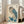May include: Japanese woodblock print style artwork of an owl with large golden eyes perched on a branch with blue-green foliage, displayed in a light wooden frame leaning against a white wall beside a beige upholstered chair in a bright room with large windows