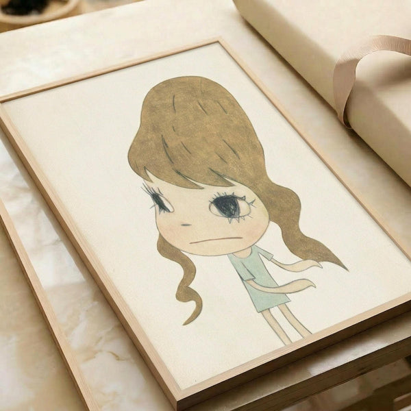 May include: Framed artwork displaying a cartoon-style illustration of a young girl with long brown wavy hair, large blue eyes, and a melancholic expression, wearing a mint green dress. The drawing has a soft, sketchy quality with muted earth tones on cream paper. The piece sits in a light wooden frame on a marble surface next to rolled white paper, creating a minimalist styling scene.