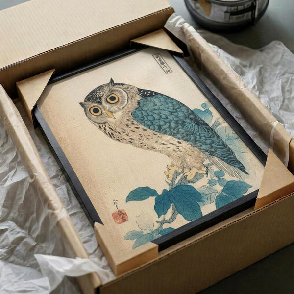 May include: Framed Japanese woodblock print of an owl with teal and blue feathers perched on flowering branches, displayed in black frame inside cardboard shipping box with protective wrapping and wooden dowels, showing vintage ukiyo-e art style with red artist seal