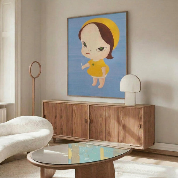 May include: Modern living room interior featuring a framed poster of a stylized cartoon child character with brown bob haircut, green eyes, wearing yellow dress and headband against blue background. The artwork hangs above a mid-century walnut credenza with sliding doors. Room includes white curved lounge chair, brass floor lamp, white table lamp, oval glass coffee table, and cream textured area rug on light hardwood floors.