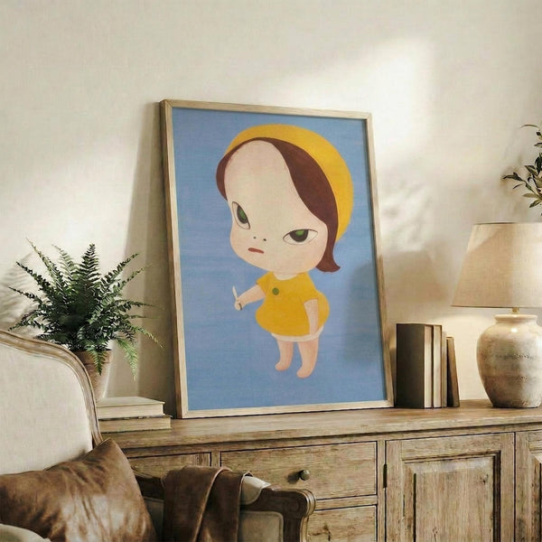 May include: Framed art print featuring a stylized illustration of a young child with brown and yellow hair wearing a bright yellow outfit, holding a small white object, set against a soft blue background. The wooden-framed artwork leans against white wall on rustic wooden sideboard, surrounded by potted plants, stacked books, ceramic vase, and brown leather furniture in warm, naturally-lit living room setting.