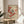 May include: Framed vintage Japanese bird illustration displayed on round wooden side table next to beige upholstered chair. Artwork features small bird with dark head and light body perched on branch with clusters of bright red berries against cream background. Natural wood frame, soft window lighting, and green plant leaves visible in corner of neutral-toned room setting.