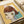 Child's drawing of a girl with brown bob haircut and large yellow-green eyes on yellow background, created with colored pencils and crayons over collaged paper fragments including pink and blue text documents, displayed as an unframed artwork on white paper