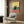 May include: Framed poster showing a grumpy black cat sitting on a coral-pink bar counter with wine glasses and bottle, against yellow and teal background. Modern living room mockup with beige armchair, geometric pillow, brass floor lamp, and dark wood wall paneling.