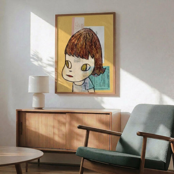 May include: Framed artwork featuring a cartoon-style child with brown bob haircut and large yellow-green eyes on yellow background with collaged text elements, displayed above a wooden mid-century credenza with white ceramic lamp, next to a sage green upholstered armchair in a sunlit room with white walls.