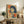 May include: Framed vintage-style poster featuring a woman with dark blue bob haircut smoking a cigarette, rendered in retro illustration style with orange and red Japanese text on cream background. Display shows rustic wooden sideboard with fern plant, stacked books, ceramic vase, and brown leather chair in modern living room setting with white walls and warm lighting.