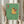 May include: Person holding framed poster showing golden retriever wearing sunglasses sitting on toilet reading magazine in green-tiled bathroom. Cartoon-style illustration with yellow dog, mint green walls and floor tiles, red toilet paper holder. Light wood frame, hands visible holding artwork, dried wheat stems and curtains in soft-lit room setting.