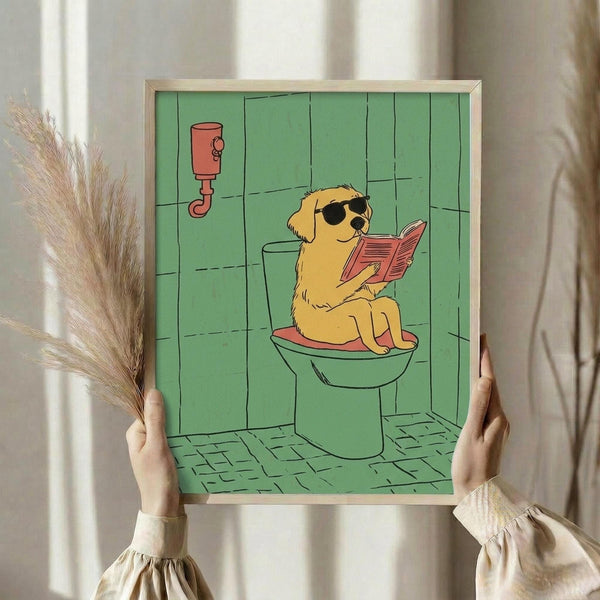 May include: Person holding framed poster showing golden retriever wearing sunglasses sitting on toilet reading magazine in green-tiled bathroom. Cartoon-style illustration with yellow dog, mint green walls and floor tiles, red toilet paper holder. Light wood frame, hands visible holding artwork, dried wheat stems and curtains in soft-lit room setting.