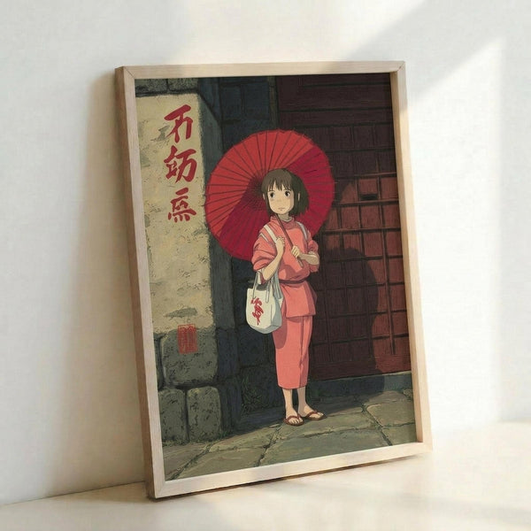 May include: Framed anime artwork showing a young girl in pink kimono holding a red parasol, standing by traditional Japanese architecture with wooden doors and stone walls. The image features Studio Ghibli animation style with warm colors and detailed backgrounds. Light wooden frame displayed against white wall.