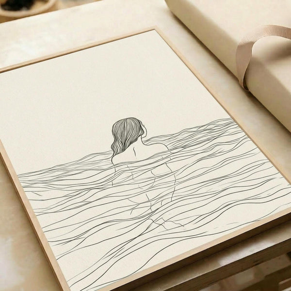 May include: Minimalist line drawing print displayed on cream paper showing a woman's head and shoulders submerged in flowing wavy lines representing water. The artwork features simple black line work on off-white background, presented in a thin wooden frame alongside wrapped gift packages in neutral tones on a light wooden surface.