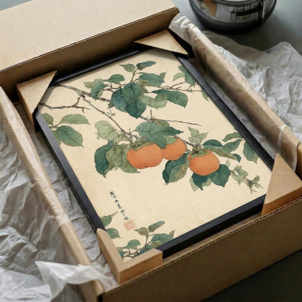 May include: Vintage Japanese botanical artwork showing orange persimmons hanging from a branch with detailed green leaves, displayed in a black frame inside an open cardboard shipping box with protective tissue paper. The print features traditional Asian calligraphy and red seal stamp in the lower left corner against a cream-colored background.