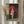 May include: Framed Studio Ghibli-style artwork showing a young girl with short brown hair in pink traditional Japanese clothing, holding a red paper umbrella and white bag, standing on stone pavement beside a building with Japanese text signage. The print is displayed in a light wood frame on a white wall next to dried pampas grass stems and flowing curtains, creating a soft, natural room setting.
