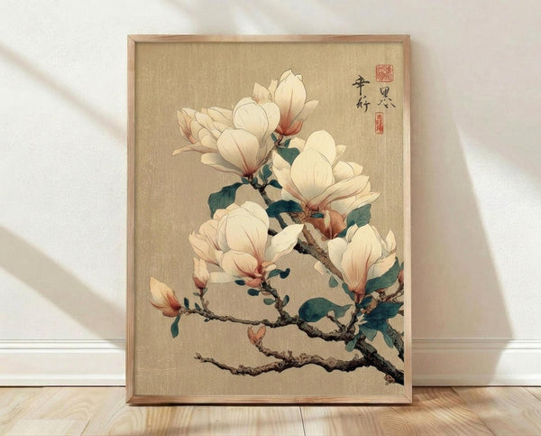 May include: Framed botanical art print showing white magnolia blossoms on dark branches against beige textured background, displayed in natural wood frame leaning against white wall on light wooden floor with soft natural lighting creating gentle shadows
