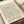 May include: A vintage-style exhibition poster featuring William Morris's intricate floral pattern in soft peach and blue tones on cream background, displayed in a light wood frame on white wrapping paper beside cream ribbon. The botanical design shows delicate trailing flowers and leaves in an all-over repeat pattern with black text announcing a cotton prints exhibition at South Kensington.