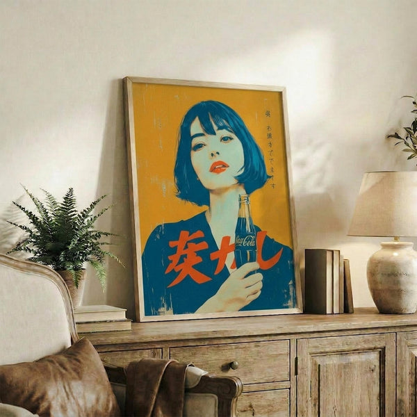 May include: Framed vintage-style Japanese Coca-Cola poster with vibrant orange background featuring woman with blue bob haircut and red lips holding classic Coke bottle, displayed on rustic wooden sideboard alongside fern plant, ceramic vase, and books in cozy living room setting with cream upholstered chair