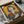 May include: Framed vintage-style Japanese Coca-Cola poster being unboxed from cardboard shipping package with protective wrapping. The retro illustration features a woman with dark bob haircut and red lips holding a Coca-Cola bottle against yellow background, with Japanese characters visible. The black-framed artwork sits nestled in brown cardboard with white tissue paper padding on a light surface.